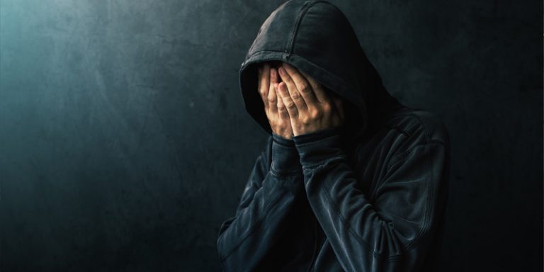 grieving, hooded man in in dark hooded jacket symbolising grief